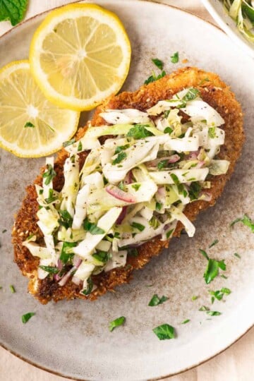 Crispy Za'atar chicken cutlet with Lebanese cabbage salad topped with fresh cabbage slaw and lemon slices on a plate.