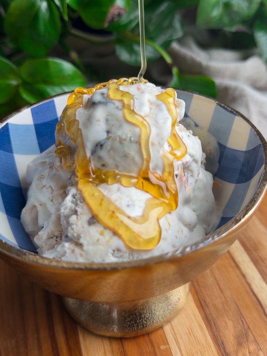 No-churn baklava ice cream topped with honey in a blue-checkered bowl on a wooden surface.