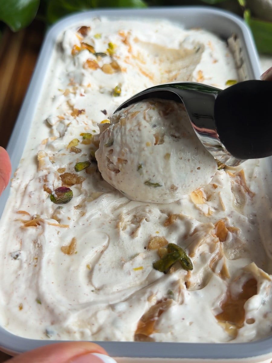 Scooping No-churn baklava ice cream with metal scoop from container.