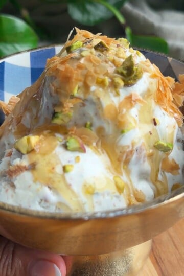 Baklava Ice Cream with honey, pistachios, and phyllo flakes in a decorative bowl on a wooden surface.