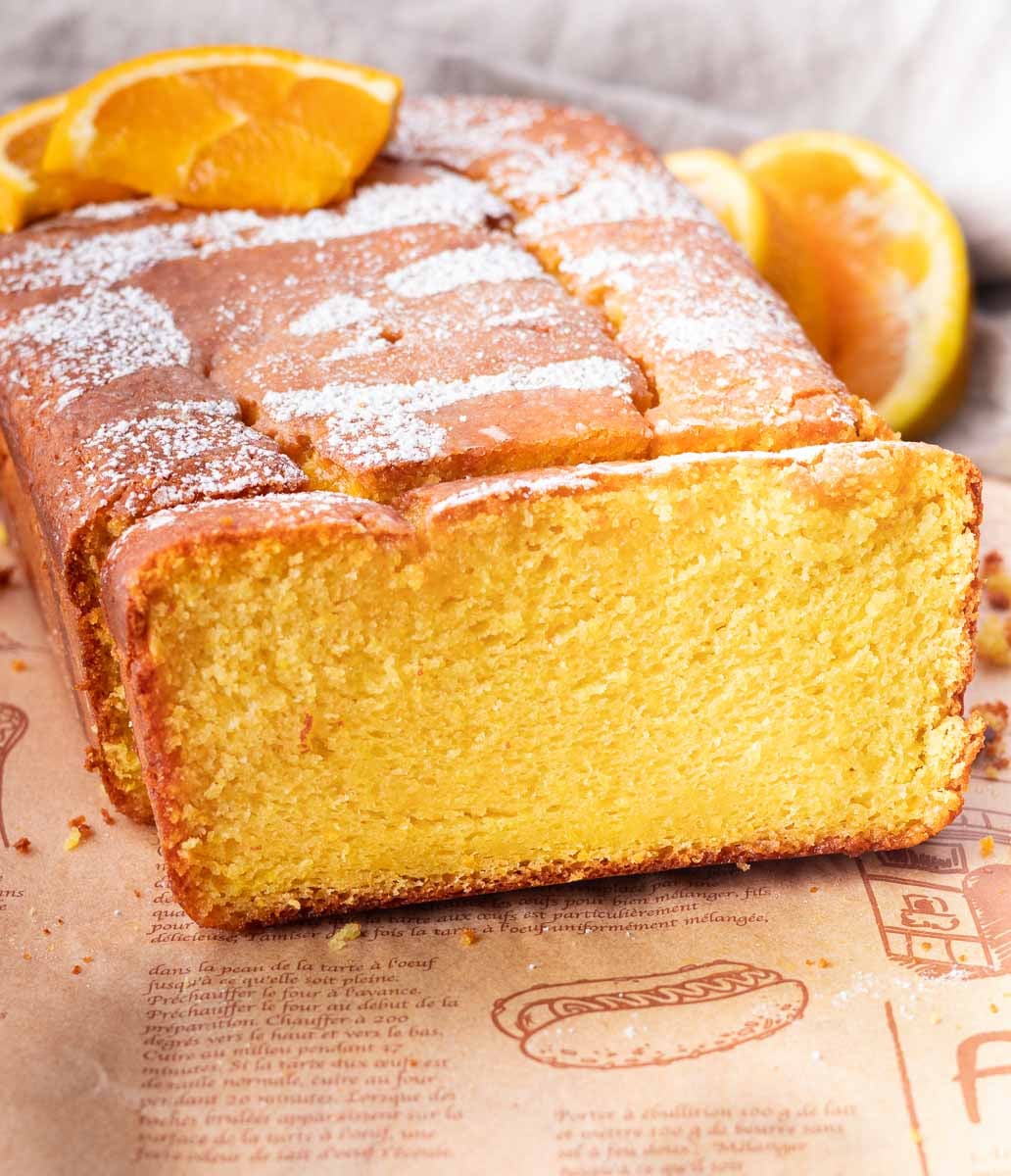 Freshly baked orange blender cake with slices on top, dusted with powdered sugar, on parchment paper.