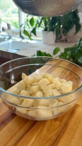 Boiled potatoes in a glass bowl on a wooden countertop.