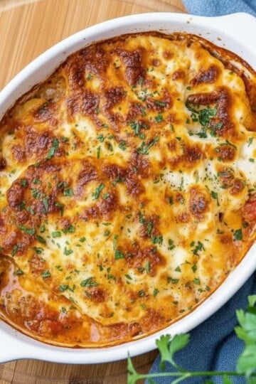 Cauliflower and chicken sausage in a white dish with a golden crust, garnished with herbs on a wooden board.