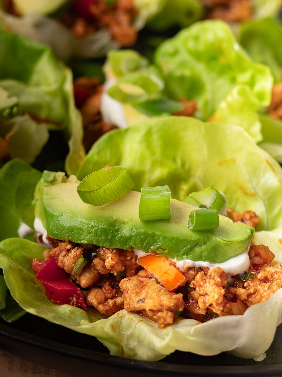 Chicken and pepper lettuce cups with chicken, avocado slices, and green onions, garnished with colorful bell peppers.