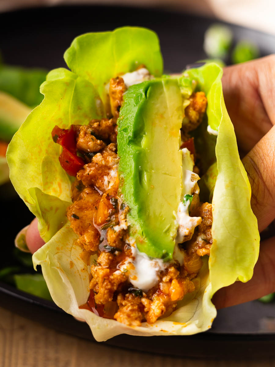 Chicken and pepper lettuce cups with seasoned ground meat, avocado, and yogurt on a black plate.