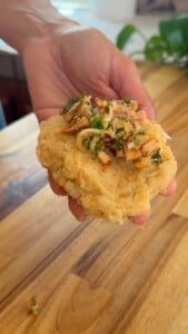Hand holding dough topped with tuna and herbs on a wooden table.