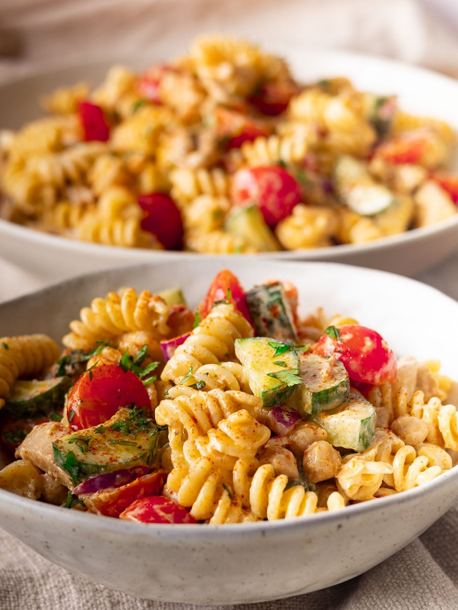 Two bowls of Mediterranean pasta salad with cherry tomatoes, cucumber, and herbs.