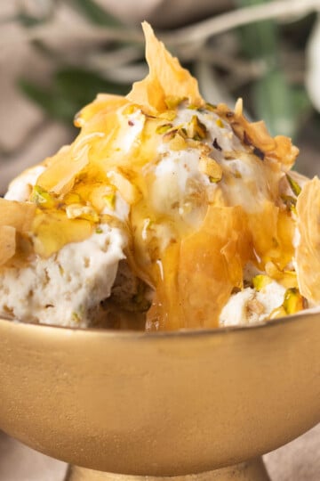 No-churn baklava ice cream, topped with honey and pistachios in a golden bowl.