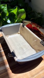 Baking tin lined with parchment paper, secured with clips, on a wooden counter.