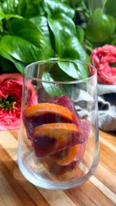Glass with frozen fruit slices on wooden surface.