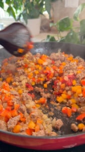 Sizzling ground lamb with diced peppers and onions in a pan, being stirred with a wooden spoon.