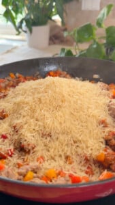 Rice atop diced vegetables and meat in a pan.