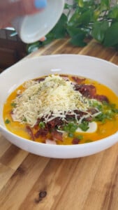Bowl of cheesy bacon, green onions, and egg mixture being seasoned on a wooden table.
