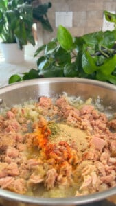 Sautéed tuna with spices in a pan, surrounded by fresh green plants on a kitchen counter.
