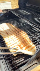 Grilling flatbread on a barbecue with tongs on a sunny day.