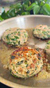 Cooking spinach chicken patties in a skillet with fresh herbs.