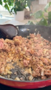 Cooking ground lamb and onions in a skillet with a wooden spoon.