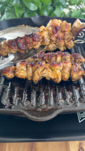 Grilled chicken skewers on a cast iron pan with metal tongs.