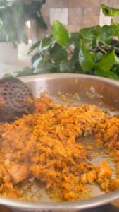 Cooking tuna in a pan with wooden spatula and green plants in the background.