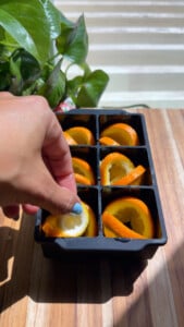 Making orange ice cubes with sliced oranges in a tray on a wooden table.