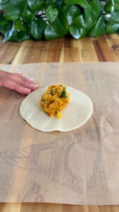Preparing empanada: dough with savory filling on parchment paper.