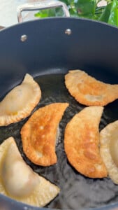 Frying crispy empanadas in a nonstick pan with golden brown texture.
