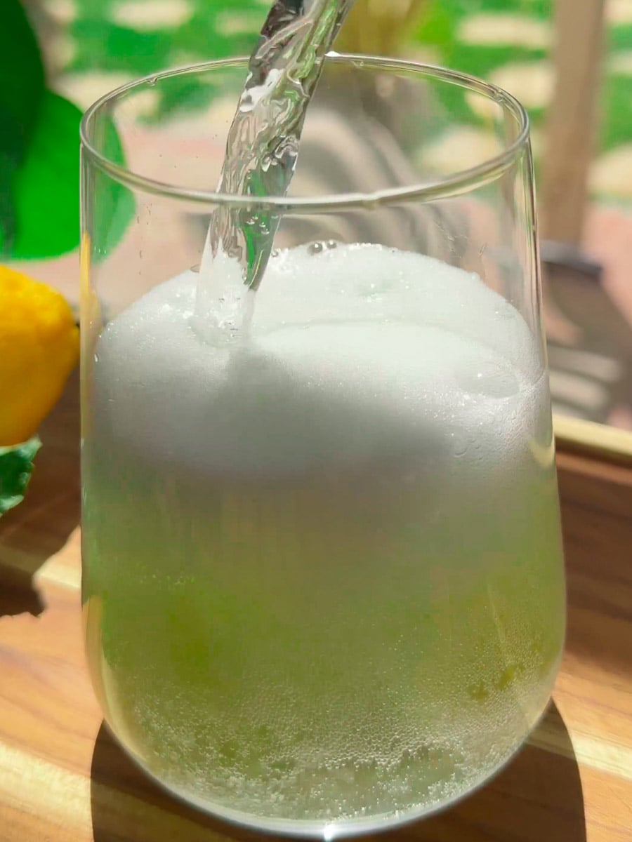 Pouring sparkling water into a glass with lemon garnish on a sunny day.