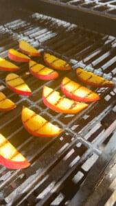 Grilled peach slices on a barbecue grill with char marks.
