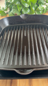 Close-up of a black grill pan with ridges on a wooden surface.