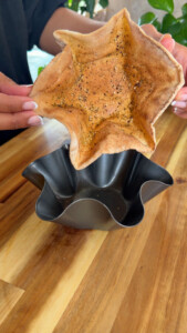Person holding a baked bread bowl over a black mold on a wooden table.