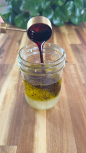 Pouring pomegranate molasses into a jar of salad dressing.