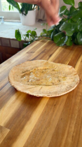 Person sprinkling seasoning on pita bread with olive oil on wooden countertop.
