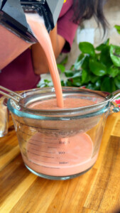 Blending pink smoothie into a measuring cup through a fine mesh strainer.