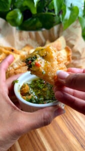 Person dipping empanada into chimichurri sauce.
