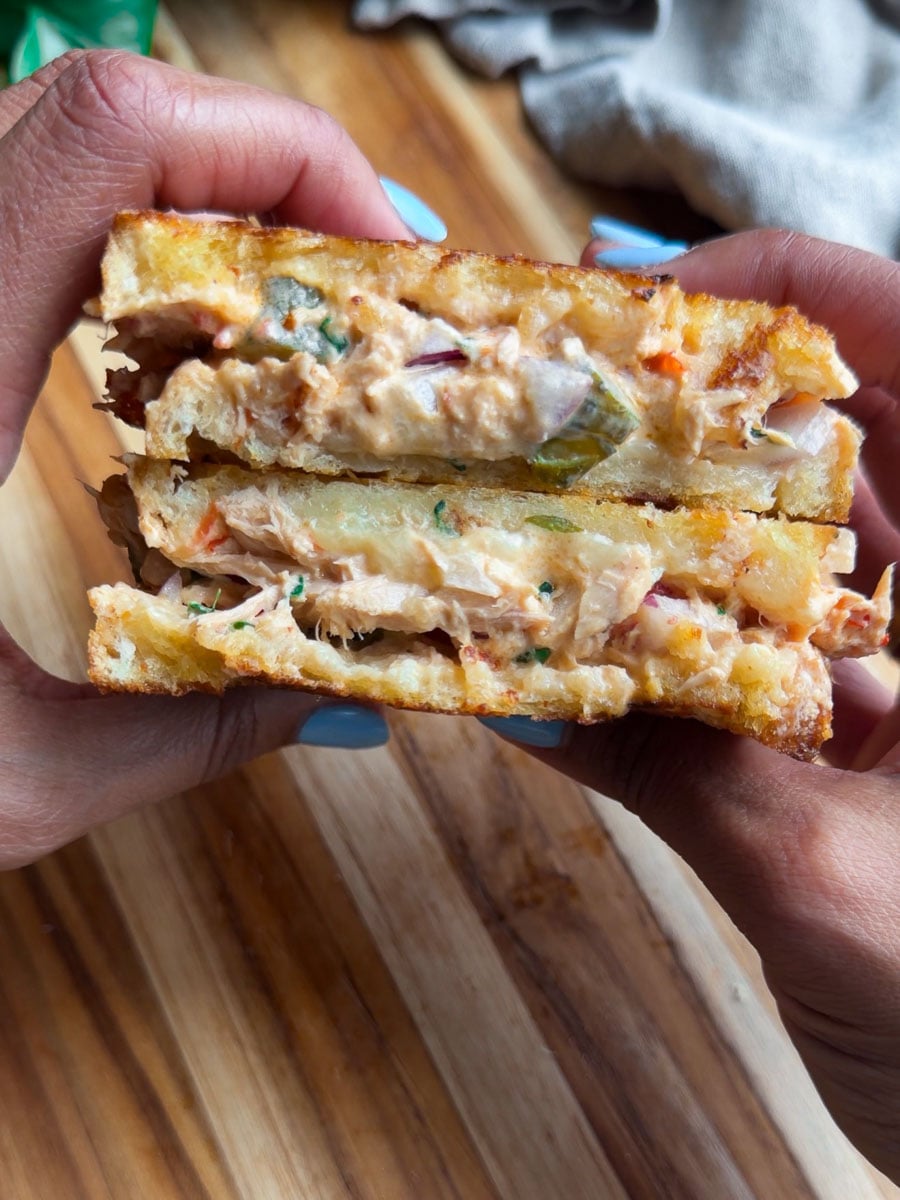 Grilled cheese sandwich with creamy filling held above wooden board.