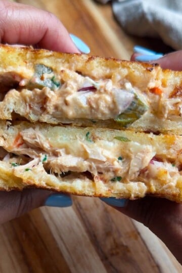 Close-up of hands holding a creamy tuna melt sandwich with toasted bread and melted cheese, showcasing a delicious cross-section.