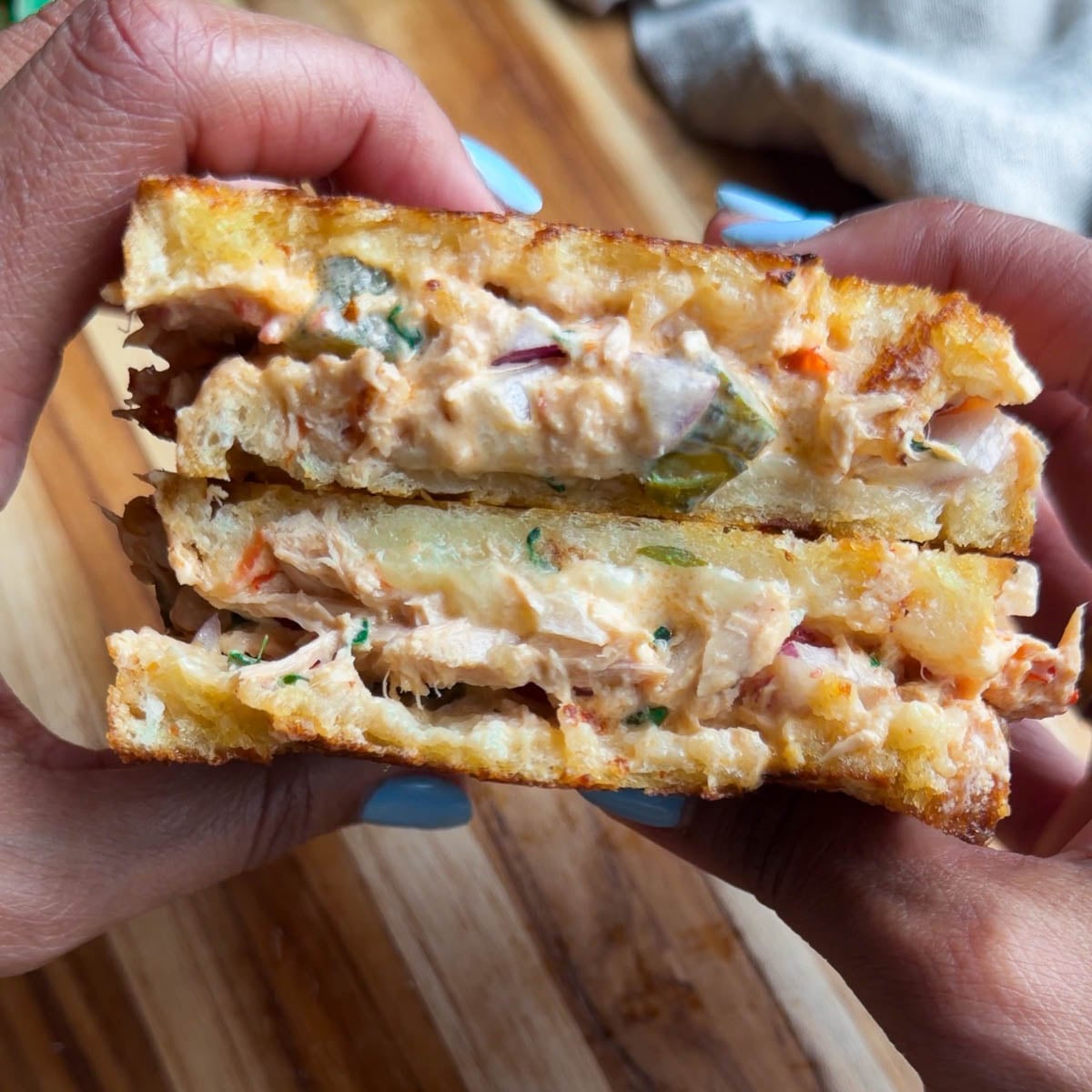 Close-up of hands holding a creamy tuna melt sandwich with toasted bread and melted cheese, showcasing a delicious cross-section.