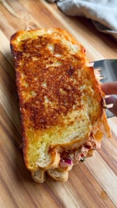 Tuna sandwich with crispy golden-brown crust on wooden board.