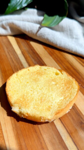 Golden toasted burger bun half on wooden board with sunlight.