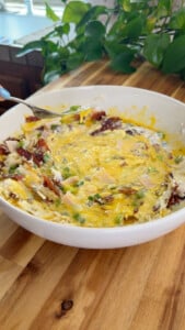 Egg mixture with bacon and other ingredients being mixed.