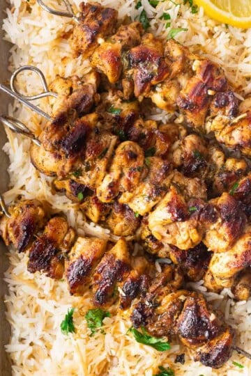 Grilled chicken pinchos morunos on a bed of rice with lemon and parsley garnish.