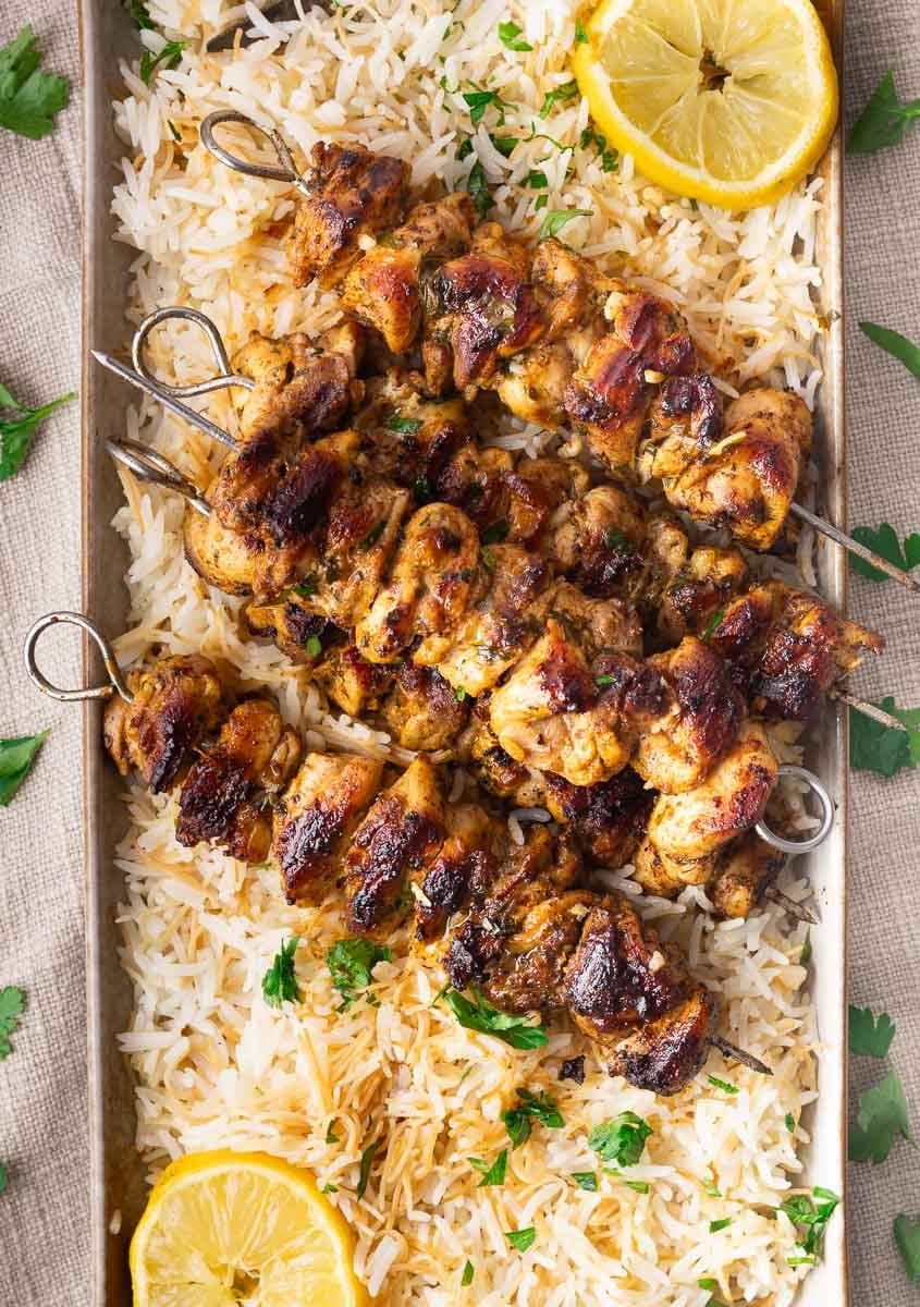 Grilled chicken skewers on a bed of rice with lemon slices and parsley garnish.