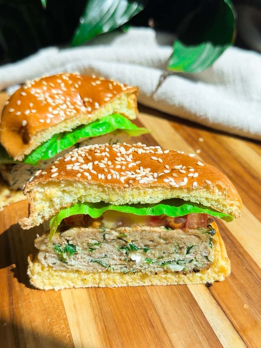 Chicken spinach burger with lettuce and tomato on sesame bun, served on wooden board.