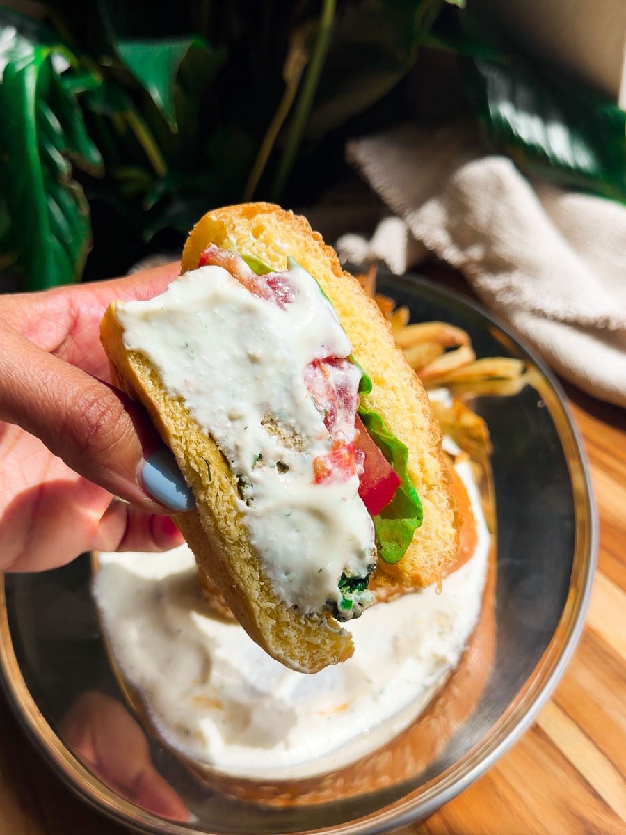 Chicken spinach burger with whipped feta and vegetables being held above a bowl on a wooden table.