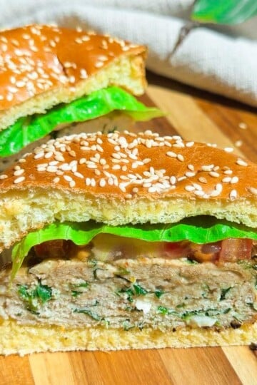 Chicken spinach burger with lettuce in a sesame seed bun on a wooden board.