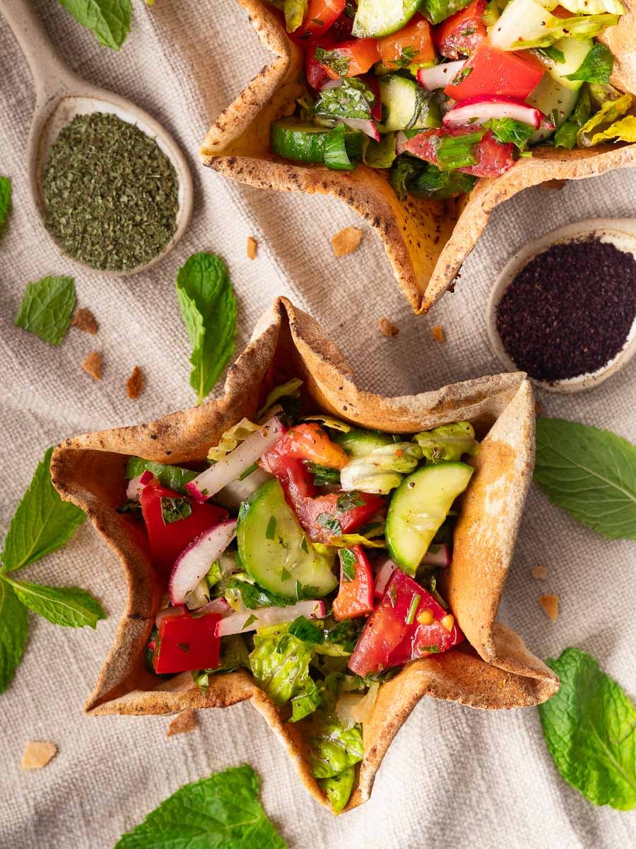 Fresh fattoush salad in a crispy pita bowl with cucumbers and tomatoes on a linen cloth.