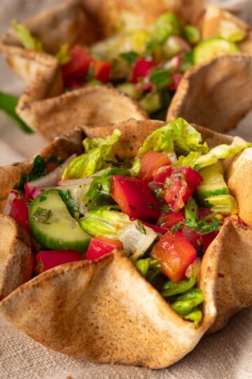 Fresh fattoush salad in a crispy pita bowl with cucumbers and tomatoes on a linen cloth.