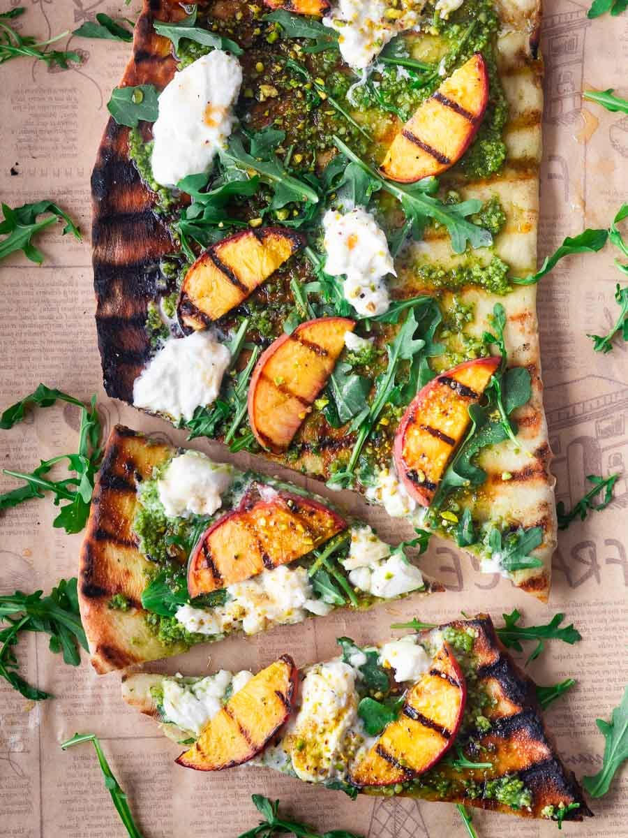 Peach burrata flatbread topped with peaches, burrata, arugula, and pesto on rustic paper.