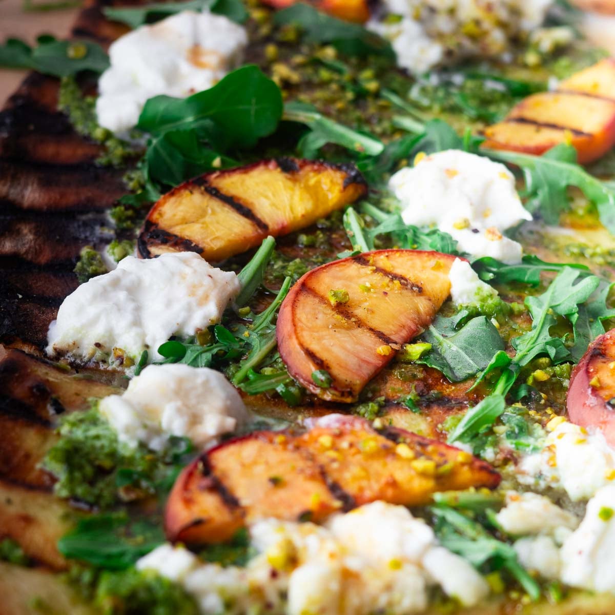 Peach burrata flatbread with grilled peach and burrata flatbread topped with arugula and pesto sauce.