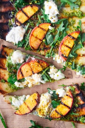 Peach burrata flatbread with peach slices, arugula, pesto, and buffalo mozzarella on rustic parchment.